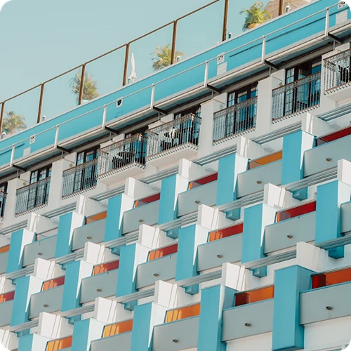 Fassade eines Geb&auml;udes mit wei&szlig;en, t&uuml;rkisfarbenen Balkonen und Metallgel&auml;ndern.